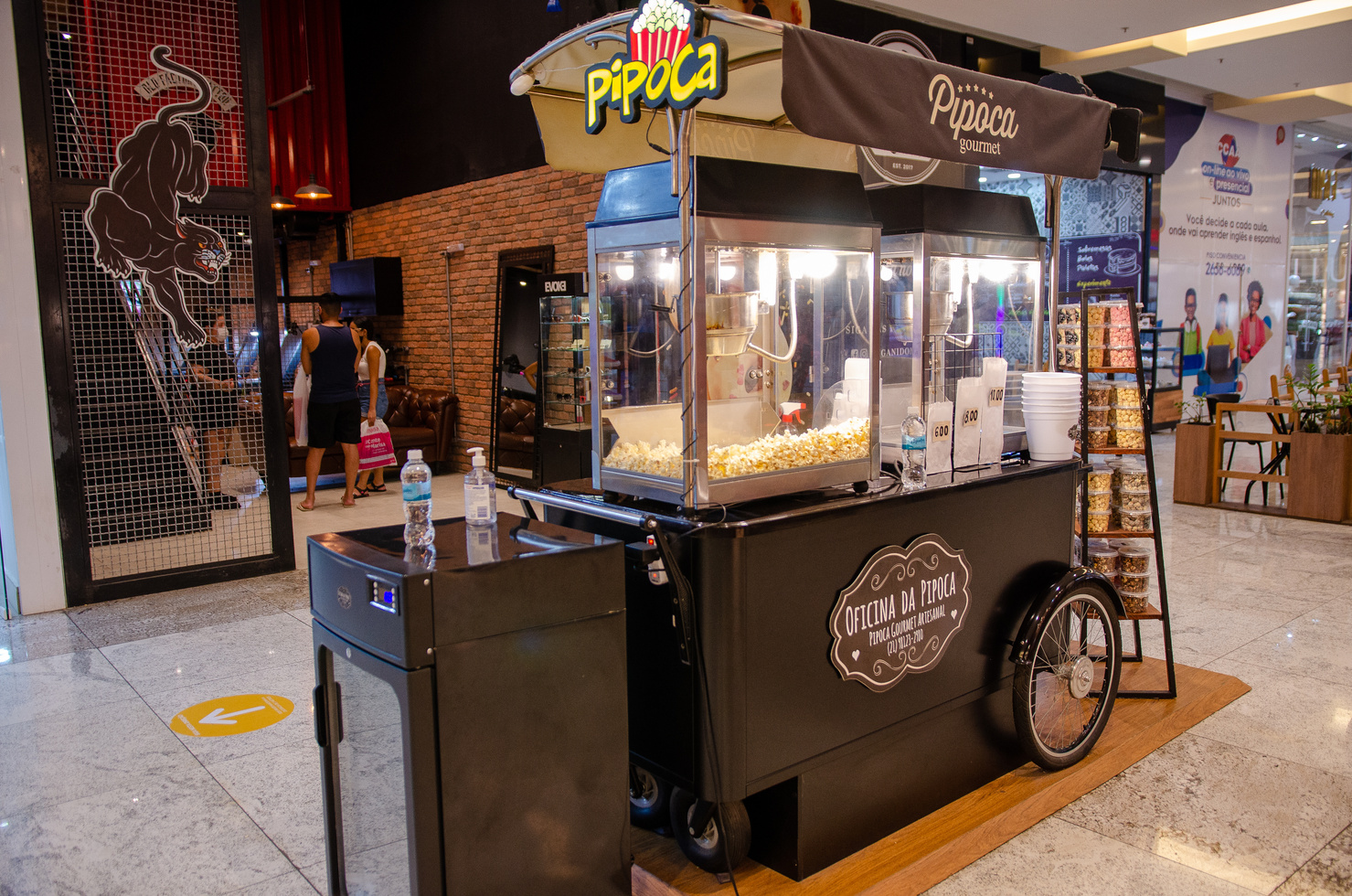 Imagem da carro agem de oficina da pipoca composta por duas fornalhas de fazer pipoca, exposta em local central, localizada no shopping Nova Iguaçu.